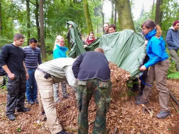 Gruppe arbeitet gemeinsam an einer Tarp-Notunterkunft aus Laub und Ästen