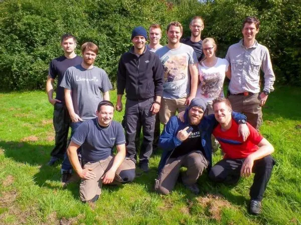 Gruppierung von zehn Personen im Freien auf einer Wiese, lächelnd und posierend