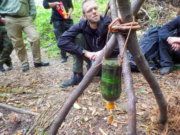 Improvisierte Wasserfilterkonstruktion hängt an einem Dreibein aus Ästen
