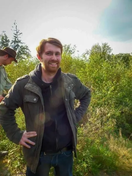 Lächelnder Mann steht in der Natur mit Händen in der Hüfte