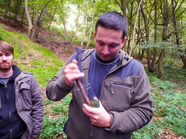 Mann bearbeitet Zunder mit einem improvisierten Werkzeug im Wald