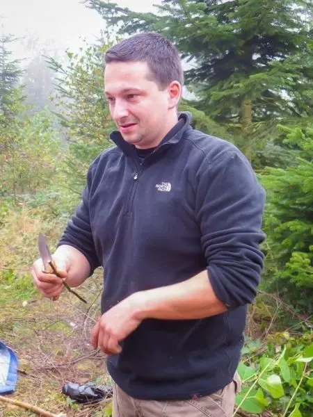 Mann hält ein Messer und bearbeitet einen Ast im Wald