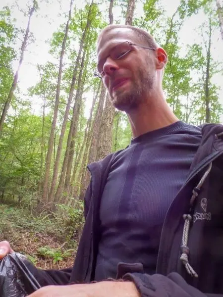 Mann hält einen schwarzen Beutel in einem Wald mit Bäumen im Hintergrund