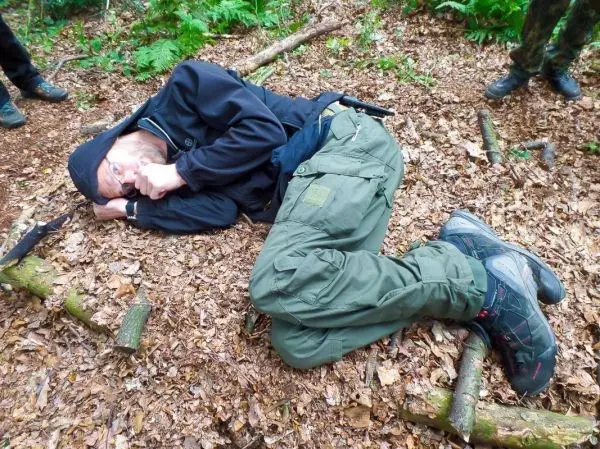 Mann liegt auf dem Boden im Wald, umgeben von Laub und Ästen