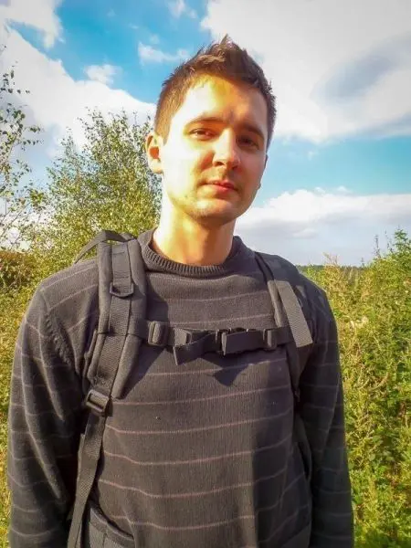 Mann mit Rucksack steht vor einer grünen Landschaft unter blauem Himmel