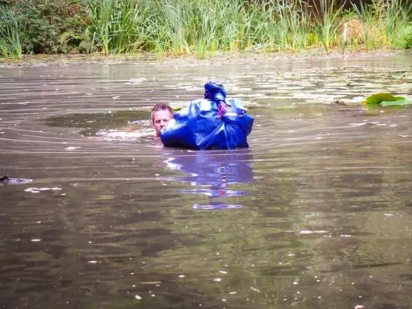 Mann schwimmt mit blauer Tasche im Wasser zwischen Pflanzen