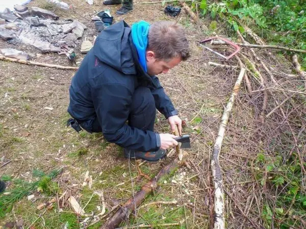 Person bearbeitet einen Stock mit einem Messer im Freien beim Survival Training