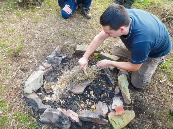 Person bereitet Feuerstelle mit trockenem Gras vor beim Survival Training
