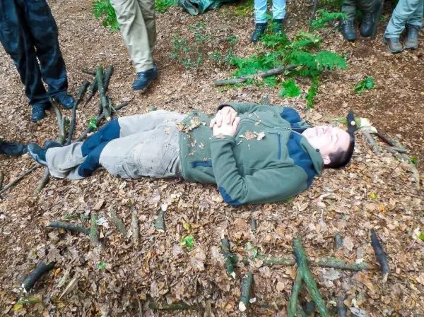 Person liegt auf dem Boden, umgeben von Blättern und Ästen
