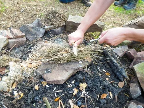 Person schichtet trockenes Gras auf einem Feuerplatz