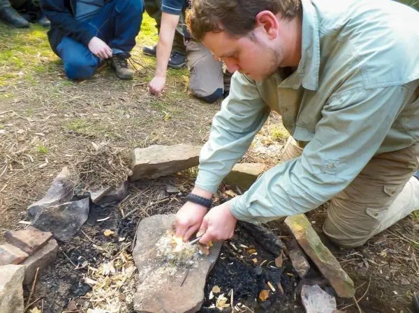 Person zündet Feuerstelle mit Zunder an beim Survival Training