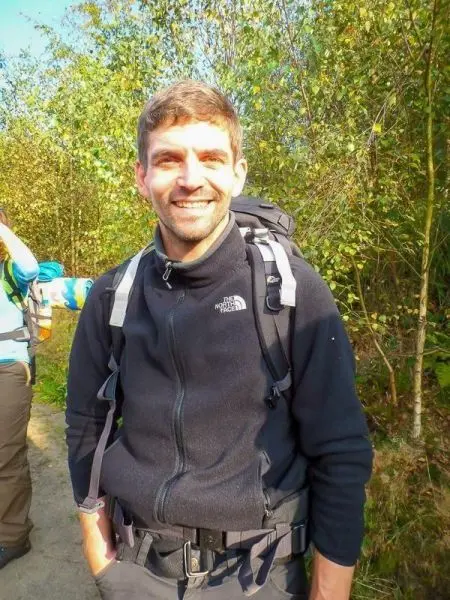 Rucksackträger lächelt vor bewaldetem Hintergrund