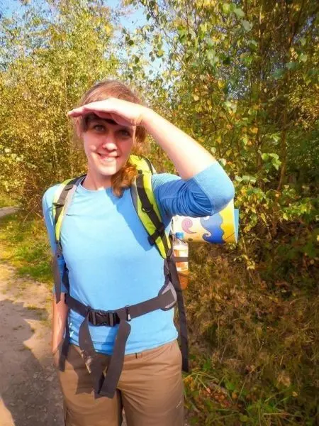 Wandernde Person mit Rucksack und Isomatte, Hand über der Stirn zum Blick in die Ferne