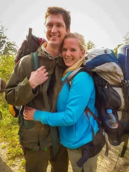 Zwei Personen mit Rucksäcken stehen umarmt in der Natur