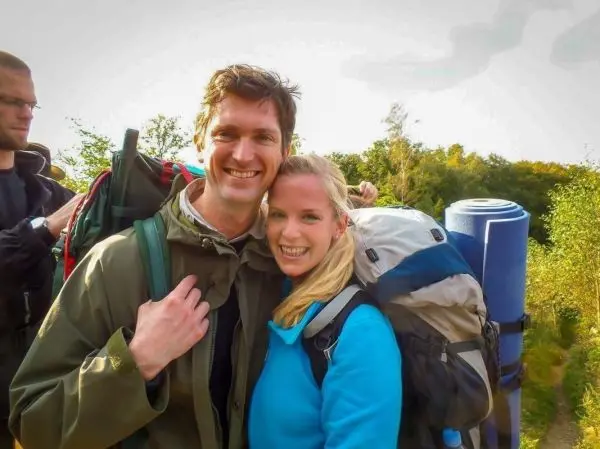 Zwei Personen mit Rucksäcken stehen vor einer grünen Landschaft