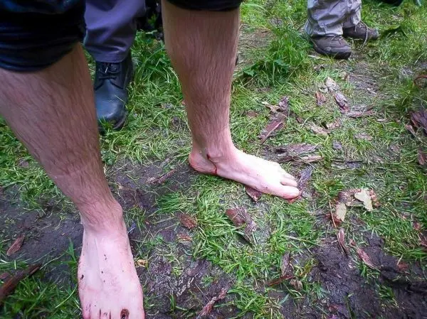 Barfüßige Beine stehen auf grünem, feuchtem Boden mit Gras und Erde