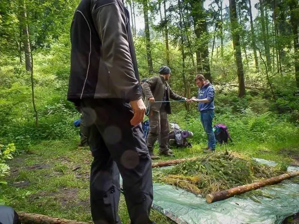 Drei Personen arbeiten an einer improvisierten Unterkonstruktion aus Ästen und Gras