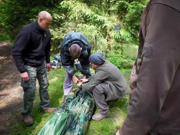 Drei Personen sichern eine Tarp-Notunterkunft auf dem Boden