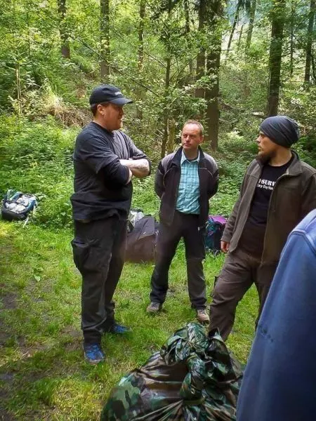 Drei Personen stehen im Wald und diskutieren, Rucksäcke liegen im Hintergrund