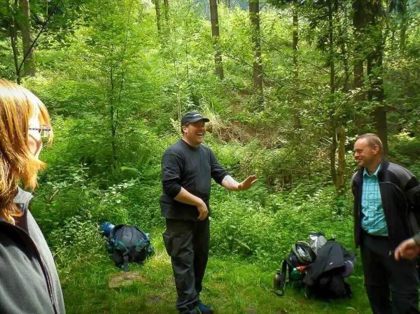 Drei Personen stehen in einem Wald, Rucksäcke liegen im Hintergrund