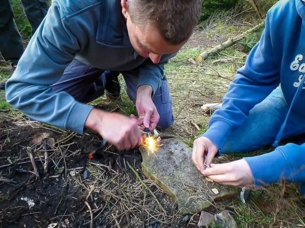 Feuerstahl erzeugt Funken auf Zunder, während zwei Personen konzentriert arbeiten