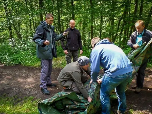 Fünf Personen bauen gemeinsam eine Tarp-Notunterkunft im Wald auf