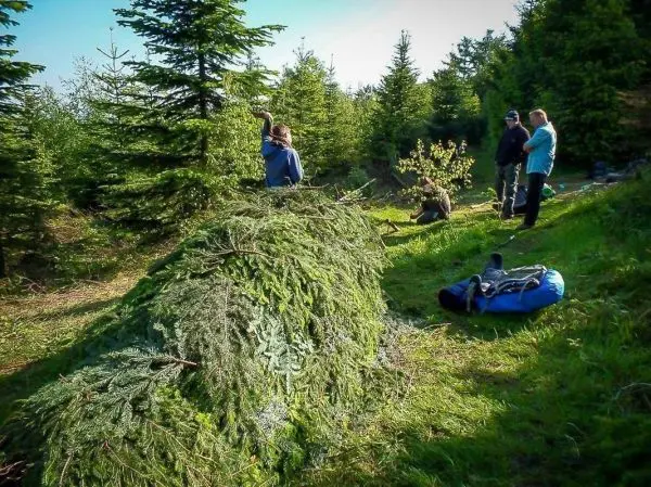 Grüne Äste bilden eine Notunterkunft, während Personen in der Nähe stehen und sich unterhalten