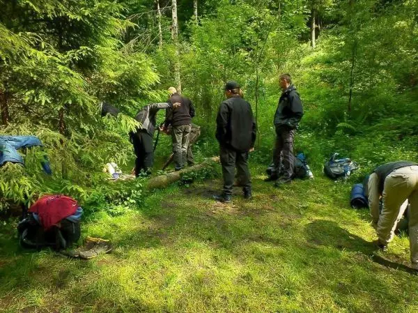 Gruppe arbeitet an einer Holzstruktur im Wald, Rucksäcke liegen verstreut