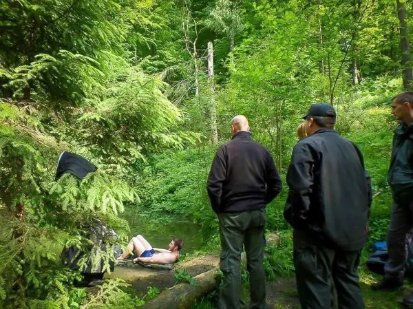 Gruppe beobachtet eine Person, die im Wasser liegt, umgeben von Bäumen und Sträuchern