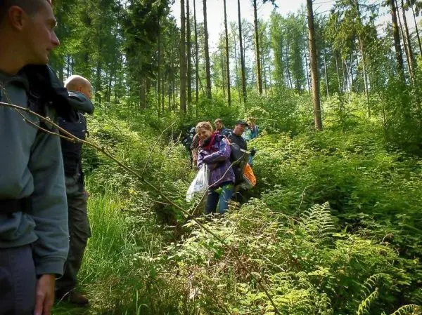 Gruppe bewegt sich durch dichten Wald mit Rucksack und Ausrüstung