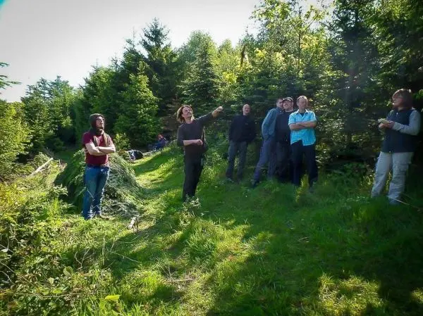 Gruppe steht auf einem Waldweg und beobachtet eine Person, die auf etwas zeigt