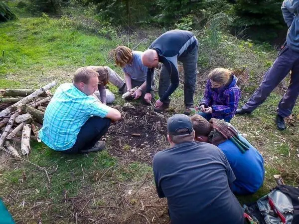 Gruppe von Personen arbeitet am Boden mit Holzstücken beim Überlebenstraining
