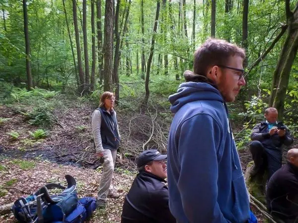 Gruppe von Personen sitzt und steht im Wald, umgeben von Bäumen und Unterholz
