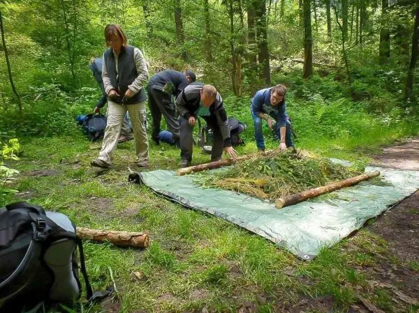 Gruppenteilnehmer bauen eine Tarp-Notunterkunft mit Ästen und Pflanzenmaterial