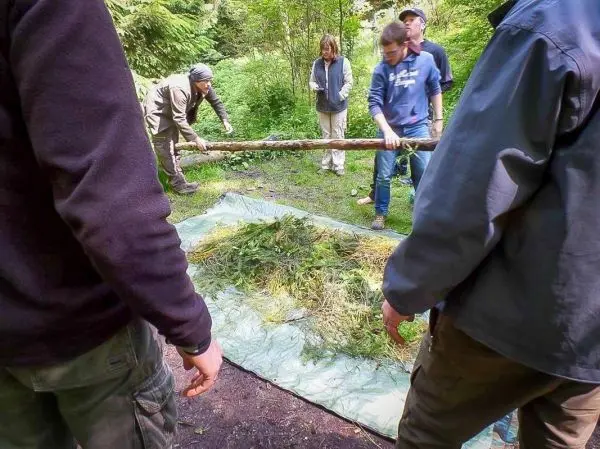 Gruppierung von Personen baut eine Tarp-Notunterkunft mit Ästen und Zunder
