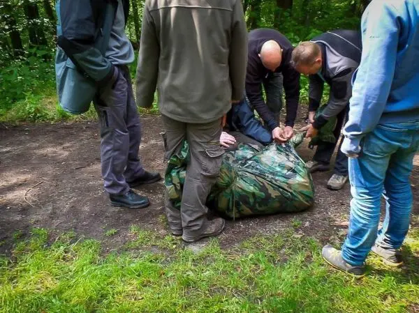 Gruppierung von Personen um einen camouflagefarbenen Sack auf dem Boden, Hände sind sichtbar