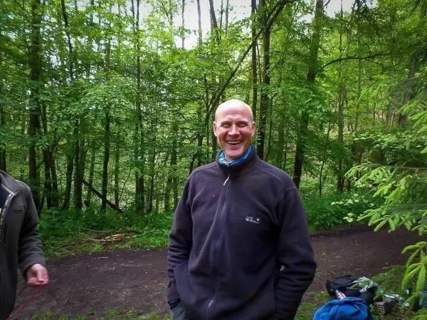 Lächelnder Mann steht im Wald, umgeben von Bäumen und grüner Vegetation