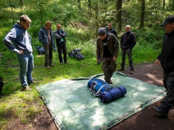 Mann entfaltet Tarp-Notunterkunft auf dem Boden, umgeben von mehreren Personen