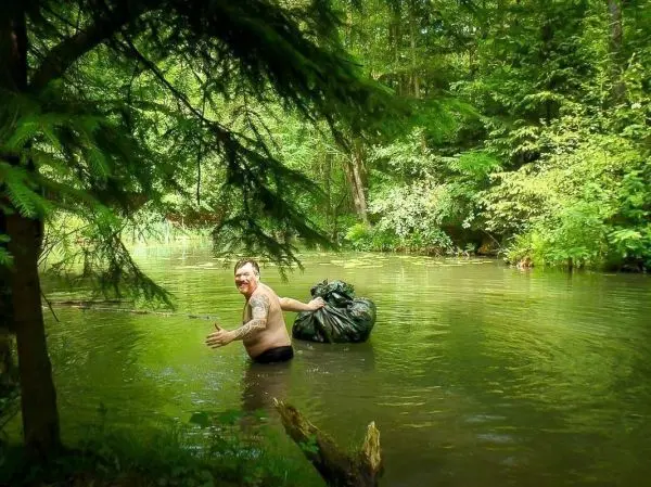 Mann im Wasser hält Müllsack und lächelt