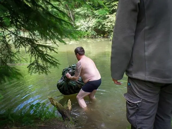 Mann im Wasser hebt einen großen, camouflagierten Sack an
