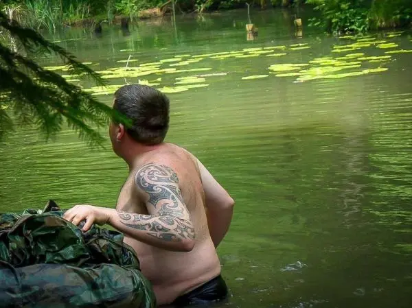 Mann im Wasser trägt eine Tasche und schaut zur Seite