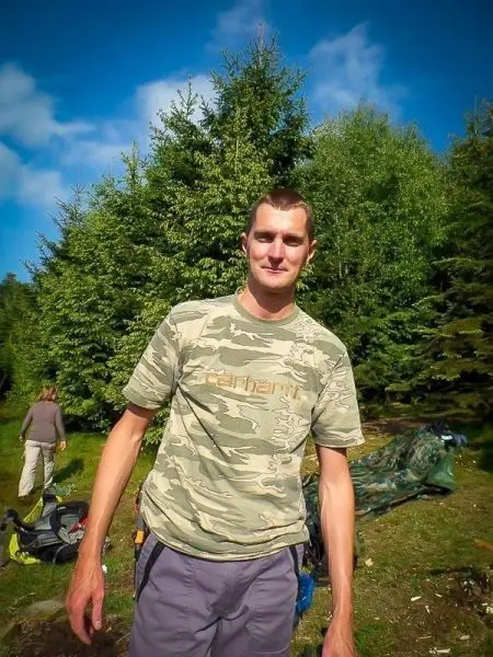 Mann in camouflierter Kleidung steht im Wald neben Ausrüstung