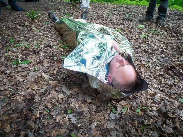 Mann liegt auf dem Boden, eingewickelt in eine Rettungsdecke aus Aluminiumfolie