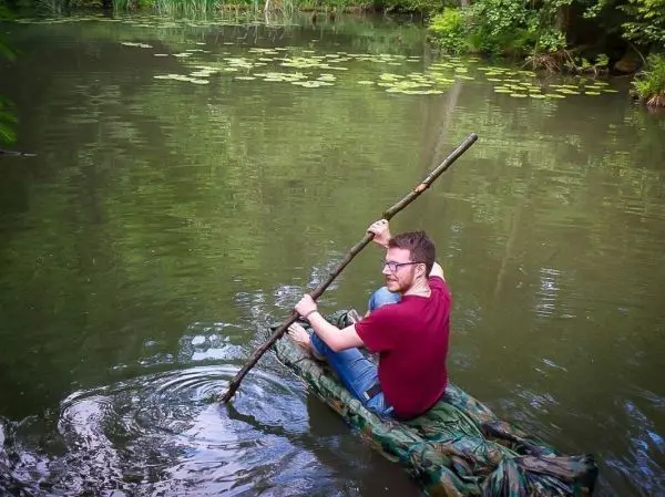 Mann paddelt auf improvisiertem Floß durch ruhiges Wasser mit Seerosen