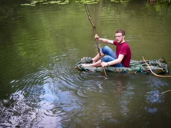 Mann paddelt auf improvisiertem Floß mit einem Stock im Wasser