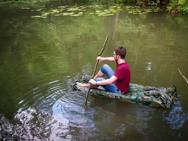 Mann paddelt auf improvisierter Bootskonstruktion aus Tuch im Wasser