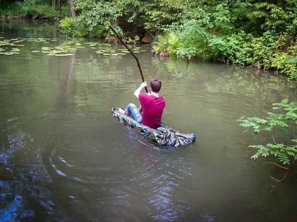 Mann paddelt mit einem Stock in einem improvisierten Boot auf einem Gewässer