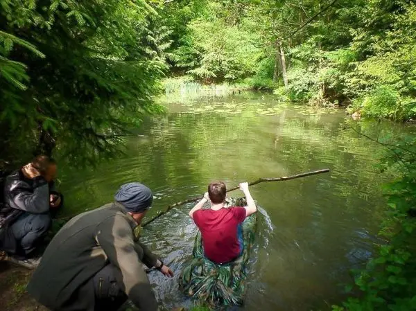 Mann paddelt mit Stock im Wasser, während zwei Personen am Ufer beobachten