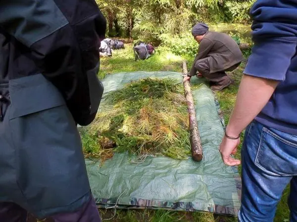 Mann platziert einen Stock auf einem mit Gras und Zweigen bedeckten Tarp