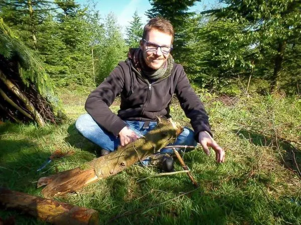 Mann sitzt auf dem Boden und arbeitet an einer Holzstruktur mit einem Messer